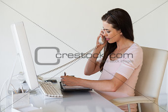 Casual pregnant businesswoman talking on phone at her desk