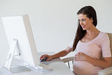 Casual pregnant businesswoman smiling at computer at her desk