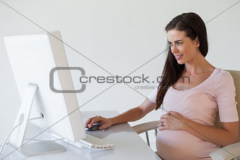 Casual pregnant businesswoman smiling at computer at her desk