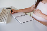 Casual pregnant businesswoman writing at her desk