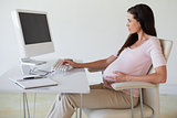 Casual pregnant businesswoman touching her bump at her desk