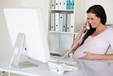 Casual pregnant businesswoman touching her bump at her desk talking on phone