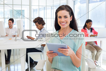 Businesswoman on tablet pc smiling at camera with colleagues behind