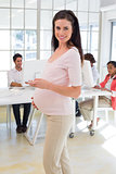 Businesswoman touches pregnancy bump while texting and smiling to camera