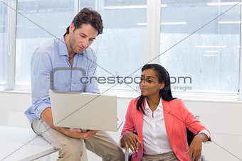Businessman showing woman in wheelchair document on laptop