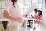 Pregnant office worker touches bump and reads document
