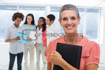 Businesswoman holds planner and smiles at camera while colleagues stand behind