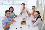 Business people eating muffins give thumbs up to camera