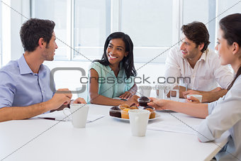 Work colleagues chatting in board room while enjoying coffee and muffins