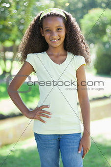 Young girl smiling at the camera in the park with hand on hip