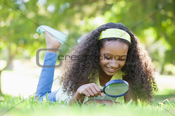 Young girl looking at grass through magnifying glass in the park