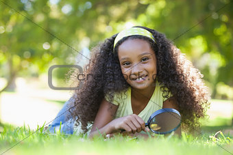 Young girl holding magnifying glass in the park smiling at camera