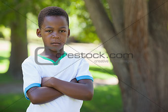 Little boy frowning at camera with arms crossed in the park