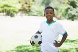 Little boy holding football in the park smiling at camera