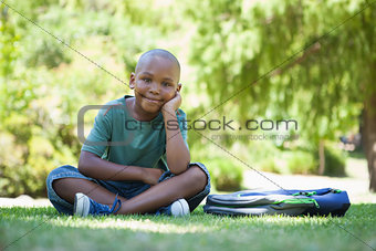 Happy schoolboy smiling at camera sitting on grass