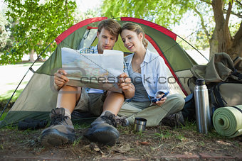 Cute couple sitting by tent reading a map