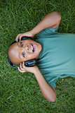 Little boy lying on grass listening to music smiling at camera