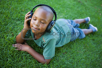 Little boy lying on grass listening to music with eyes closed