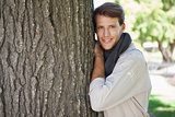 Handsome man leaning against tree smiling at camera