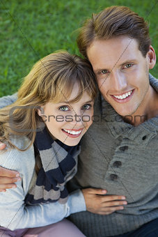 Cute couple sitting in the park embracing smiling at camera