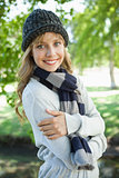 Pretty blonde in hat and scarf smiling at camera in the park