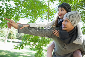 Man giving his pretty girlfriend a piggy back and pointing in the park