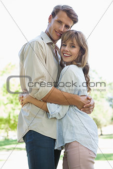 Carefree couple standing in the park and hugging smiling at camera