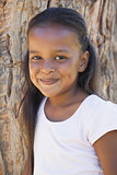 Little girl by large tree smiling at camera