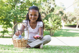 Little girl sitting on grass counting easter eggs smiling at camera