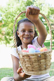 Little girl sitting on grass showing basket of easter eggs to camera