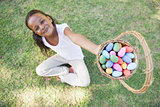Little girl sitting on grass showing basket of easter eggs to camera