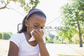 Little girl sitting on grass blowing her nose