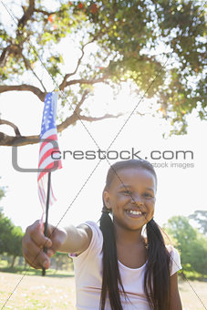 Little girl sitting on grass waving american flag