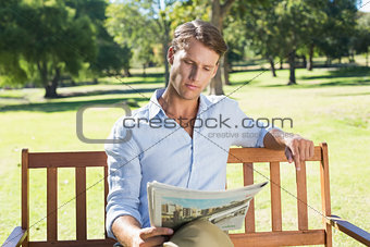 Handsome man sitting on park bench reading newspaper