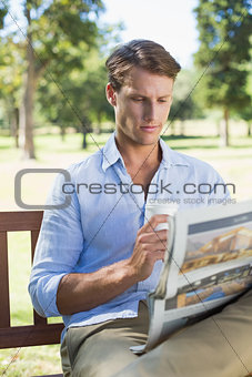 Man sitting on park bench drinking coffee and reading paper