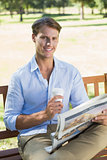 Smiling man sitting on park bench drinking coffee and reading paper