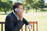 Casual businessman talking on phone on park bench with coffee