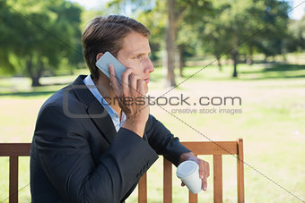 Casual businessman talking on phone on park bench with coffee