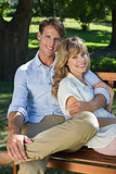 Affectionate couple relaxing on park bench together smiling at camera