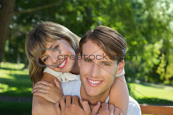 Cute couple embracing in the park smiling at camera