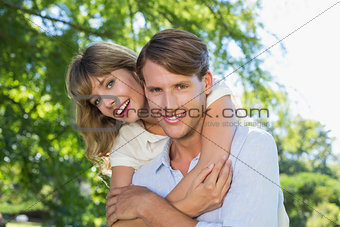 Man giving his pretty girlfriend a piggy back in the park smiling at camera