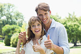 Attractive couple smiling at camera and showing thumbs up in the park