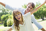 Attractive couple smiling at camera and spreading arms in the park