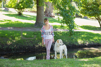 Pretty smiling blonde walking with her labrador in the park