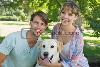 Happy couple sitting with their labrador in the park smiling at camera