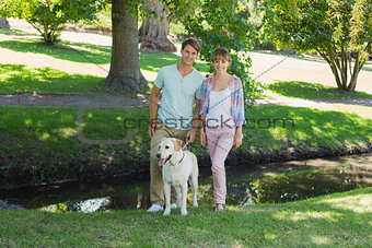 Happy couple standing with their labrador in the park smiling at camera