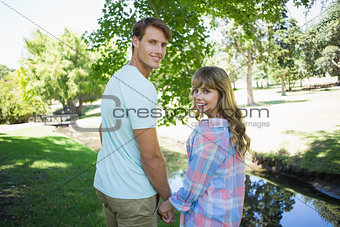 Cute couple walking hand in hand in the park smiling at camera