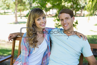 Cute couple sitting on bench in the park smiling at camera