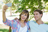 Cute couple sitting on bench in the park taking a selfie