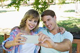 Smiling couple sitting on bench in the park taking a selfie